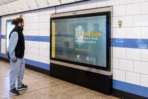 A member of the public, is looking at an LED panel in an underground station, in London, which says over 473 million children live in areas affected by conflict.